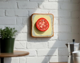 May include: A slice of toast with a yellow spread and a red tomato slice. The toast is set against a white brick wall, with a small potted plant and a coffee maker in the background. The artwork is a whimsical food-themed piece.