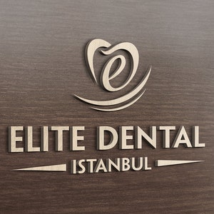 May include: A three-dimensional logo sign featuring the text ELITE DENTAL ISTANBUL in a light beige, metallic finish. Above the text is a stylized icon resembling a tooth with a lowercase letter e inside, all set against a dark wood grain background.