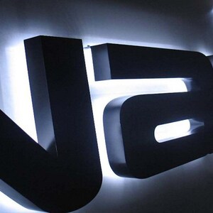 May include: Black 3D sign with white LED lights spelling out the word "VAU"