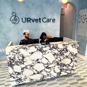 May include: A reception desk with a black and white marble pattern stands in front of a light blue wall featuring the text URvet Care. Two people and a small dog are positioned behind the desk, which is illuminated by two hanging pendant lights.
