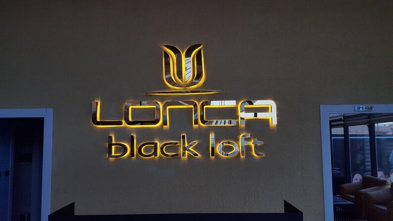 May include: A gold-coloured sign with the text "LONCA black loft" in a modern font. The sign is illuminated with warm yellow lights.