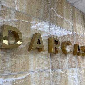 In this picture, on a shiny marble-clad wall, there is a sign reading “DARCASE” in shiny gold metal letters.