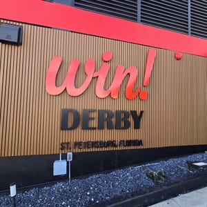 Puede incluir: Un exterior de edificio con una pared de listones de madera verticales y letreros tridimensionales. La palabra win! est&aacute; en letra cursiva roja grande, seguida de la palabra DERBY en letras negras y St. Petersburg, Florida en texto negro.