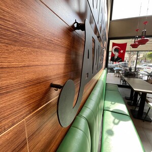 May include: Interior shot of a restaurant with a wooden wall featuring a large, black metal sign. A long, green leather bench runs along the wall. A Turkish flag hangs in the background.