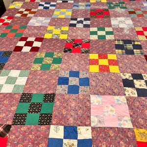 May include: A patchwork quilt featuring a repeating nine-patch block design. The quilt is composed of various fabric squares in diverse colors including red, yellow, green, blue, and pink, interspersed with floral and plaid patterned fabric blocks.