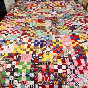 Peut inclure: Une grande courtepointe en patchwork composée d'une grille dense de petits carrés de tissu multicolores. La courtepointe présente une grande variété de motifs, notamment des fleurs, des pois, des carreaux et des couleurs unies en rouge, jaune, bleu, vert et rose.