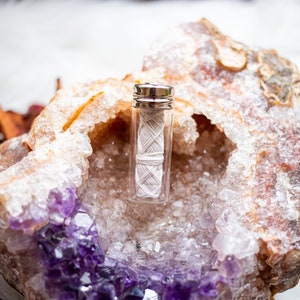 May include: A small glass jar with a silver lid containing white dental floss, resting inside a hollowed-out amethyst geode.