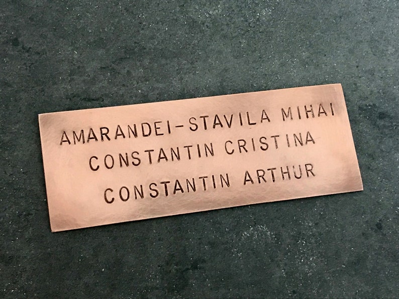 May include: A copper-colored rectangular plaque with the names "Amarandei-Stavila Mihai", "Constantin Cristina", and "Constantin Arthur" engraved in a serif font.