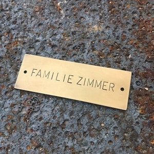 Pu&ograve; includere: Un cartello per porte in ottone con il testo "FAMILIE ZIMMER" in lettere nere.