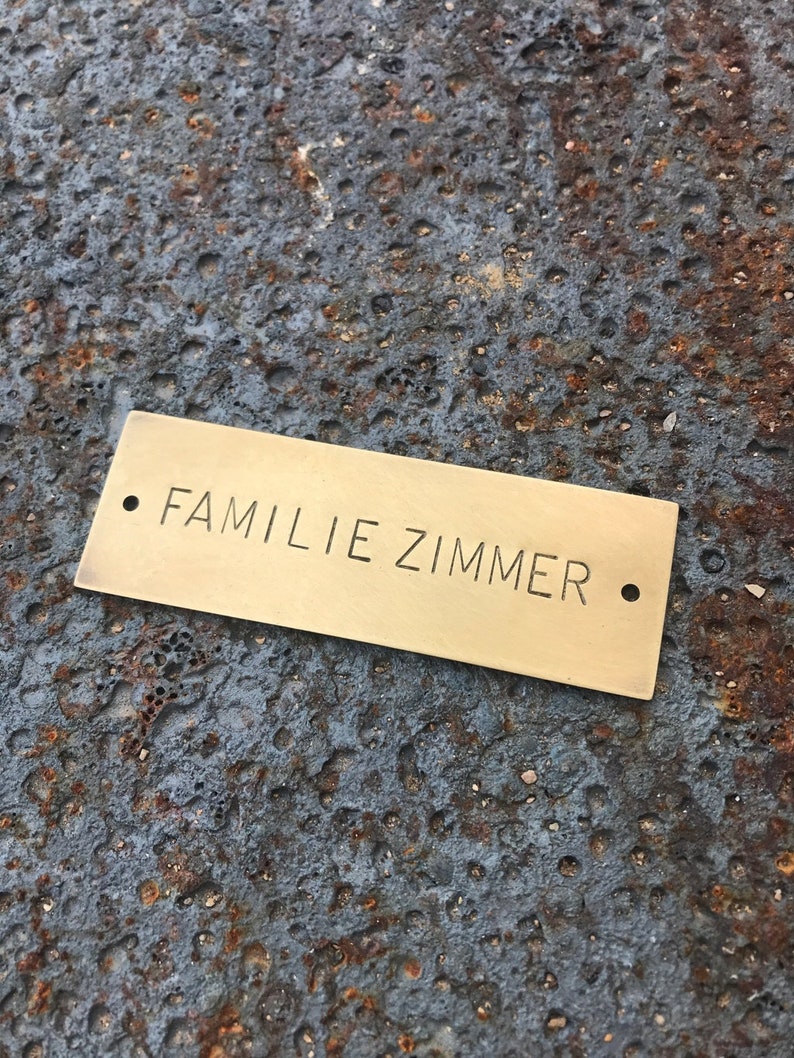 Pu&ograve; includere: Un cartello per porte in ottone con il testo "FAMILIE ZIMMER" in lettere nere.