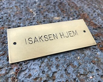 May include: A brass plaque with the text "ISAKSEN HJEM" engraved on it. The plaque has two holes on the top and bottom.