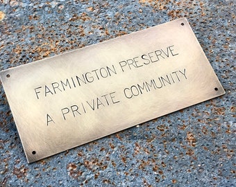 May include: A brass plaque with the text "Farmington Preserve A Private Community" engraved on it. The plaque has a brushed finish and is mounted on a rusty surface.
