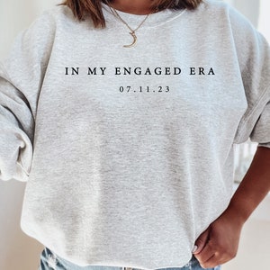May include: Gray sweatshirt with the text "IN MY ENGAGED ERA 07.11.23" printed on the front.