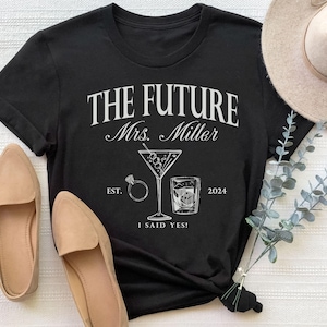 May include: Black t-shirt with white text that reads "The Future Mrs. Miller Est. 2024 I Said Yes!"  The shirt also features a martini glass with olives and a shot glass with ice.
