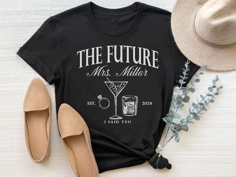 May include: Black t-shirt with white text that reads "The Future Mrs. Miller Est. 2024 I Said Yes!"  The shirt also features a martini glass with olives and a shot glass with ice.