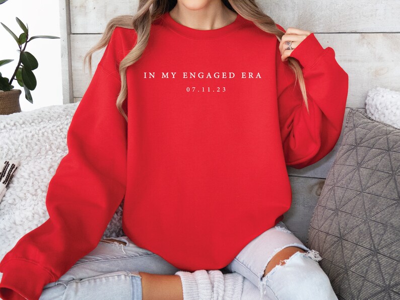 May include: Red sweatshirt with white text that reads "In my engaged era 07.11.23".