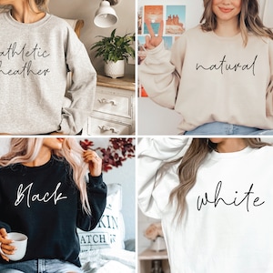 May include: Four different colored sweatshirts with the words "athletic heather", "natural", "black", and "white" written in cursive on them.