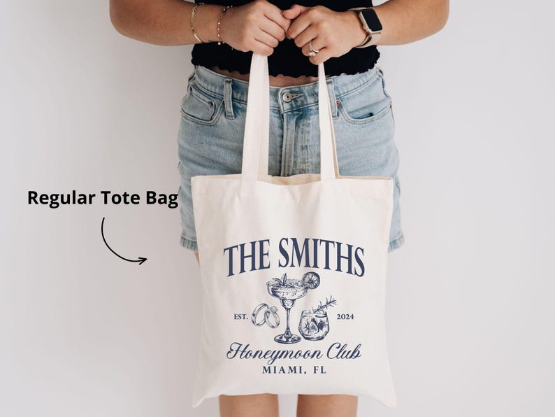 May include: Cream-colored tote bag with navy blue text and illustrations. The bag features the words "THE SMITHS" above a cocktail and other graphics, with "Honeymoon Club" and "MIAMI, FL" below. The year "2024" is also printed on the bag.