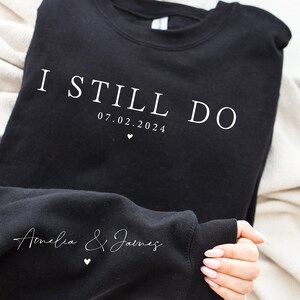 May include: Black sweatshirt with white text that reads "I Still Do 07.02.2024" and "Amelia & James" with a small heart symbol.