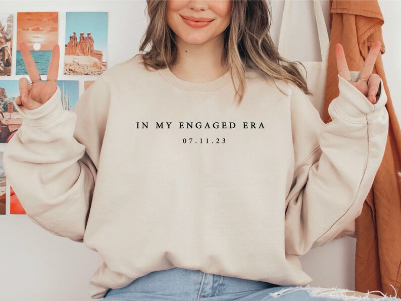 May include: A beige sweatshirt with the text "IN MY ENGAGED ERA 07.11.23" printed on the front.