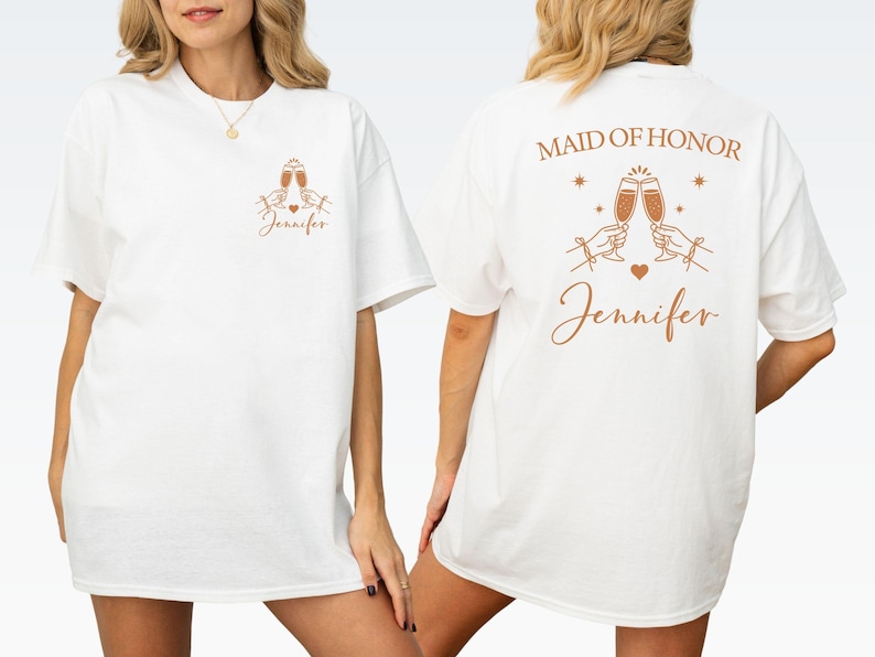 May include: White t-shirt with a front and back design. The front features two champagne glasses, a heart, and the name "Jennifer" in a script font. The back says "Maid of Honor" above the same champagne glasses and name.