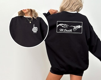 May include: Black sweatshirt with white trim and a skeleton hand graphic giving the middle finger. The back features a white rectangular design with skeleton hands and the text "Til Death". A casual, gothic-themed apparel item.