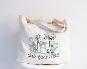 Könnte beinhalten: Eine cremefarbene Stofftasche mit einem dunkelgrünen Grafikdruck von einer Palme, einem Sonnenschirm, einem Trinkbecher, einer Sonnenbrille und Muscheln. Der Text lautet Miami, Florida, Amelia's Bachelorette, Est. 2026 und Girls Gone Mild.