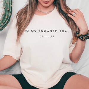 May include: A white t-shirt with the text "IN MY ENGAGED ERA 07.11.23" printed on the front.