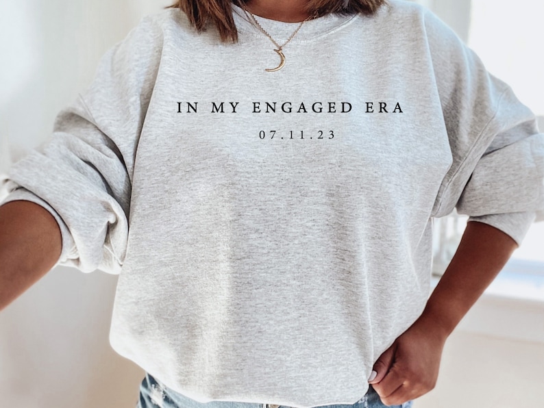 May include: Gray sweatshirt with the text "IN MY ENGAGED ERA 07.11.23" printed on the front.