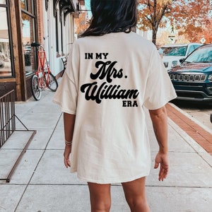 May include: A white t-shirt with the text "In My Mrs. William Era" printed in black on the back.