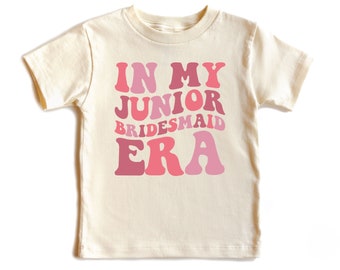 May include: A white short-sleeved t-shirt with the text "In My Junior Bridesmaid Era" in pink and red retro-style lettering.