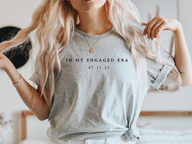 May include: A gray t-shirt with the text "In My Engaged Era 07.11.23" printed on the front.