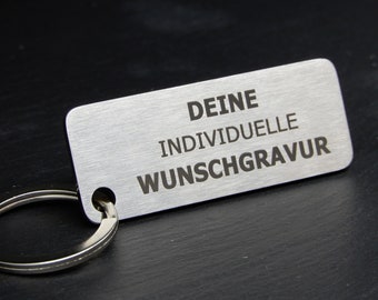May include: A silver metal keychain with a rectangular tag that reads "DEINE INDIVIDUELLE WUNSCHGRAVUR".