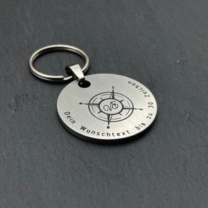 Peut inclure: Un porte-cl&eacute;s en argent avec un design de boussole et le texte "Dein Wunschtext bis zu 30 Zeichen".
