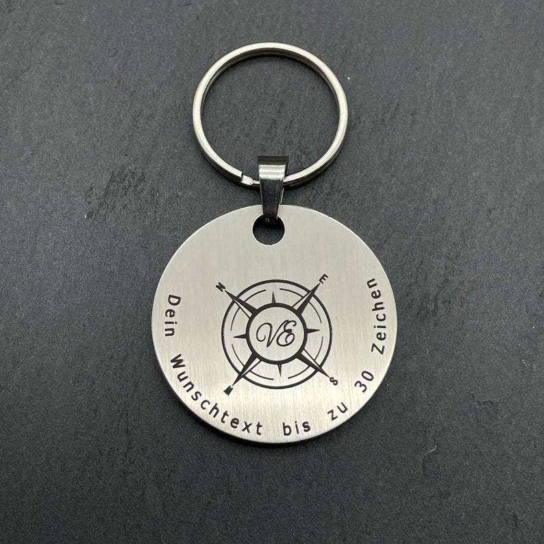 Peut inclure: Un porte-cl&eacute;s en argent avec un motif de boussole et le texte "Dein Wunschtext bis zu 30 Zeichen".