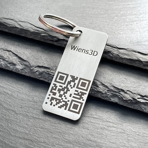 Könnte beinhalten: Ein silberner Schlüsselanhänger mit einem schwarzen QR-Code und dem eingravierten Text "Wiens3D".