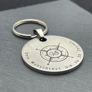 Peut inclure: Porte-cl&eacute;s en argent avec un design de boussole et le texte "Dein Wunschtext bis zu 30 Zeichen".