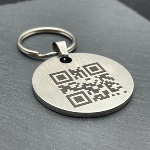 Könnte beinhalten: Ein silberner Schlüsselanhänger mit einem runden Anhänger, auf dem ein schwarz-weißer QR-Code abgebildet ist. Der Schlüsselanhänger hat einen silbernen Ring.