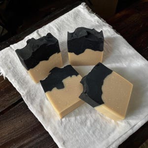 May include: Four bars of handmade soap with a black and white swirl design. The soap is on a white cloth background.