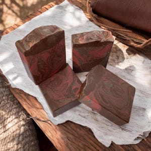 May include: Four bars of handmade soap with a marbled brown and red design. The soap is on a white surface.