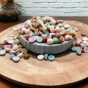 May include: A bowl filled with colorful candy, some of the candy is broken in half, and the candy is scattered on a wooden surface.