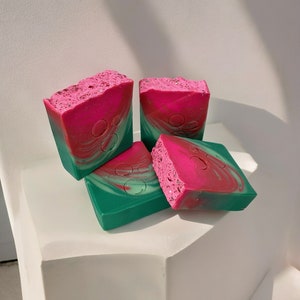 May include: Four bars of handmade soap, two are pink and green swirl, two are green and pink swirl. The soap is on a white surface.