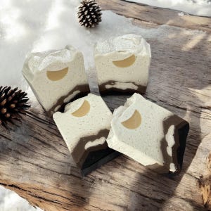 May include: Four handmade soap bars with a white base and brown swirls. Each bar has a gold crescent moon design.