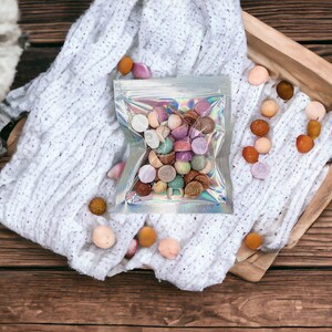 May include: A clear plastic bag filled with colorful round candies. The bag is sitting on a white knitted blanket with more candies scattered around it.