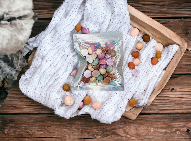 May include: A clear plastic bag filled with colorful round candies. The bag is sitting on a white knitted blanket with more candies scattered around it.