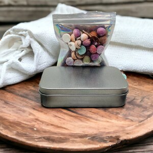 May include: A wooden tray with a silver metal tin, a white cloth, and a clear plastic bag filled with colorful candy.