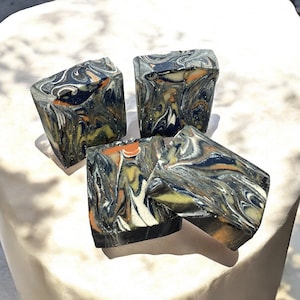 Op de afbeelding: Vier handgemaakte zeepjes met een zwart, wit en oranje marmerpatroon.