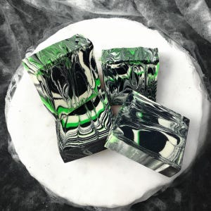 Può includere: Quattro saponette fatte a mano con un design marmorizzato nero, bianco e verde. Il sapone è su una superficie bianca.