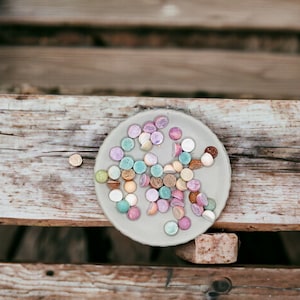 May include: A close-up of a plate of colorful candy. The candy is arranged in a circle on a light gray plate. The candy is a variety of colors, including pink, blue, green, and yellow.