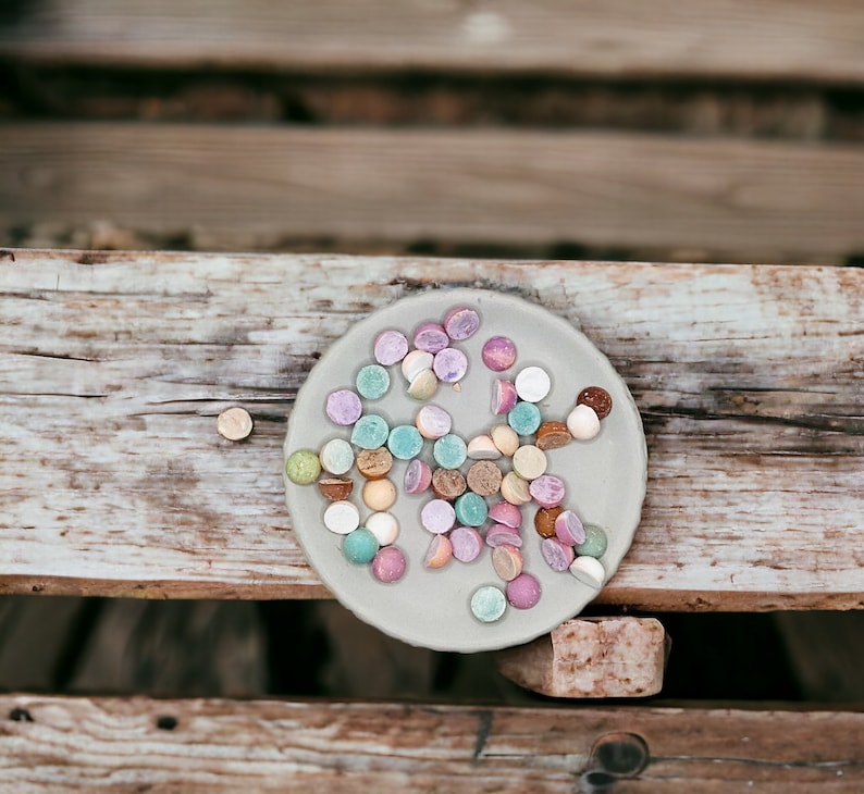 May include: A close-up of a plate of colorful candy. The candy is arranged in a circle on a light gray plate. The candy is a variety of colors, including pink, blue, green, and yellow.